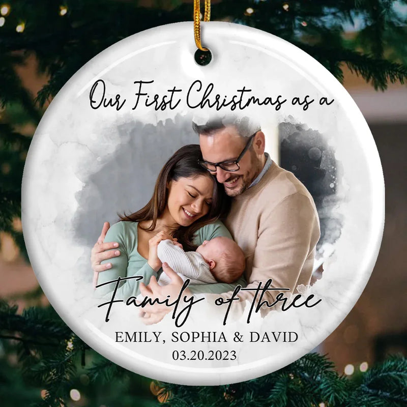 Custom Photo Our First Christmas As A Family Of Three - Couple Personalized Custom Ornament - Ceramic Round Shaped - Christmas Gift For Husband Wife, Anniversary, First Christmas